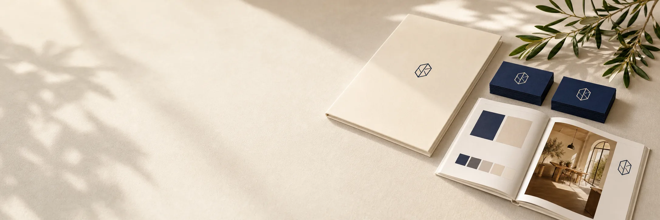 A logo on a cream folder, navy business cards and an open brand guide on a linen table